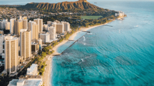 Aerial shot of a beach in Hawaii beside a city and a mountain.