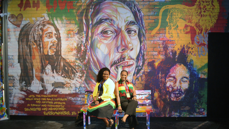 Ann Shaw, The Travel Agent Next Door (L) and Sandra Williams-Reid, TTI Travel in front of a Bob Marley mural at the Bob Marley One Love Experience.